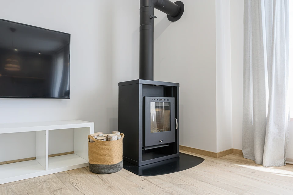 Le salon moderne est doté d'un poêle à bois noir, d'une télévision, d'une étagère blanche et d'une corbeille de bois, le tout sur un parquet en bois clair