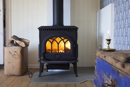 Intérieur domestique avec poêle à bois noir en fonte installé, feu allumé visible à travers la vitre ornementale