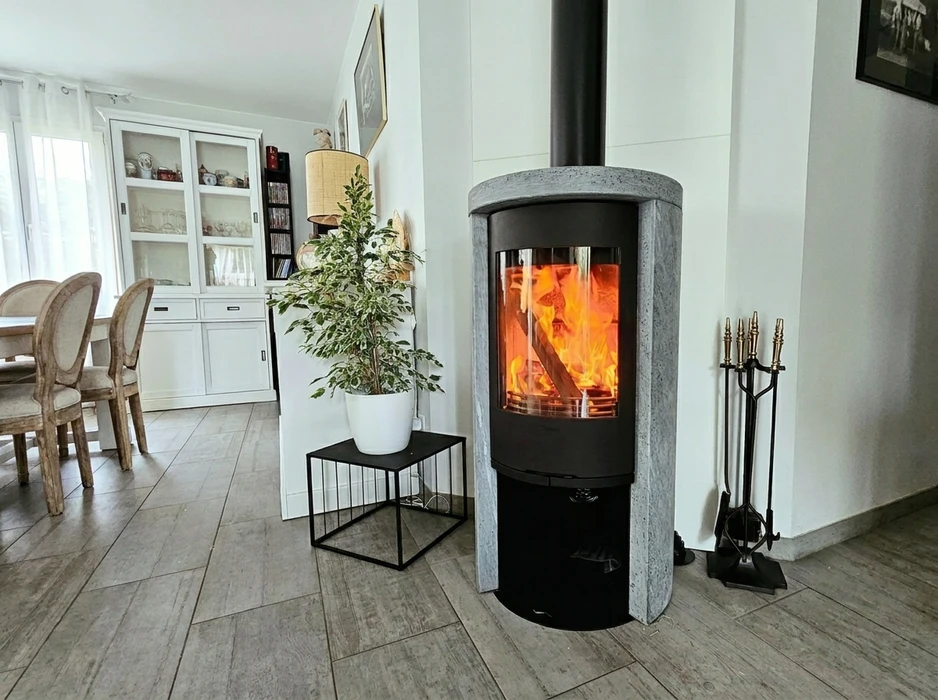 Salon moderne avec poêle à bois cylindrique en fonte noire et habillage en pierre naturelle grise, tuyau de fumée noir apparent