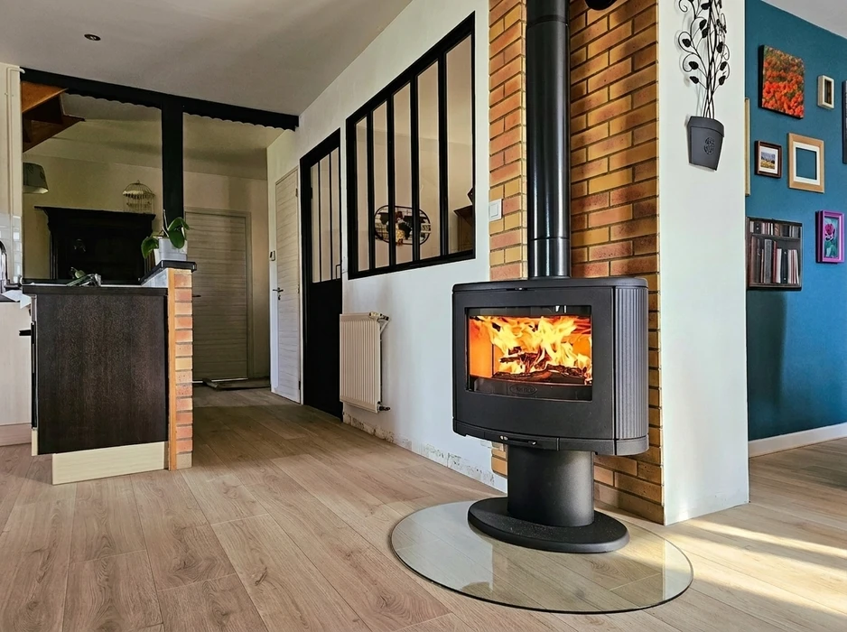 Intérieur moderne avec poêle à bois sur socle central, fonte noire, vitre panoramique révélant des flammes vives