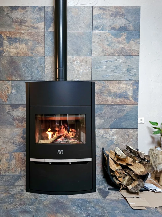 Salon moderne avec poêle à bois en fonte noire, vitrage bombé, feu actif visible, cuivre sur les poignées