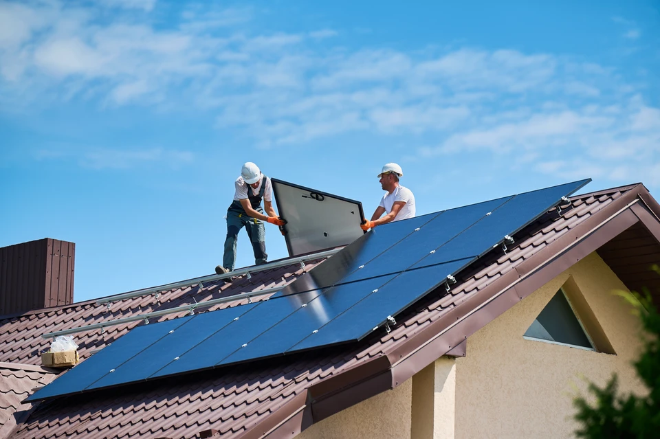 Deux techniciens installent des panneaux solaires photovoltaïques sur une toiture résidentielle par temps ensoleillé