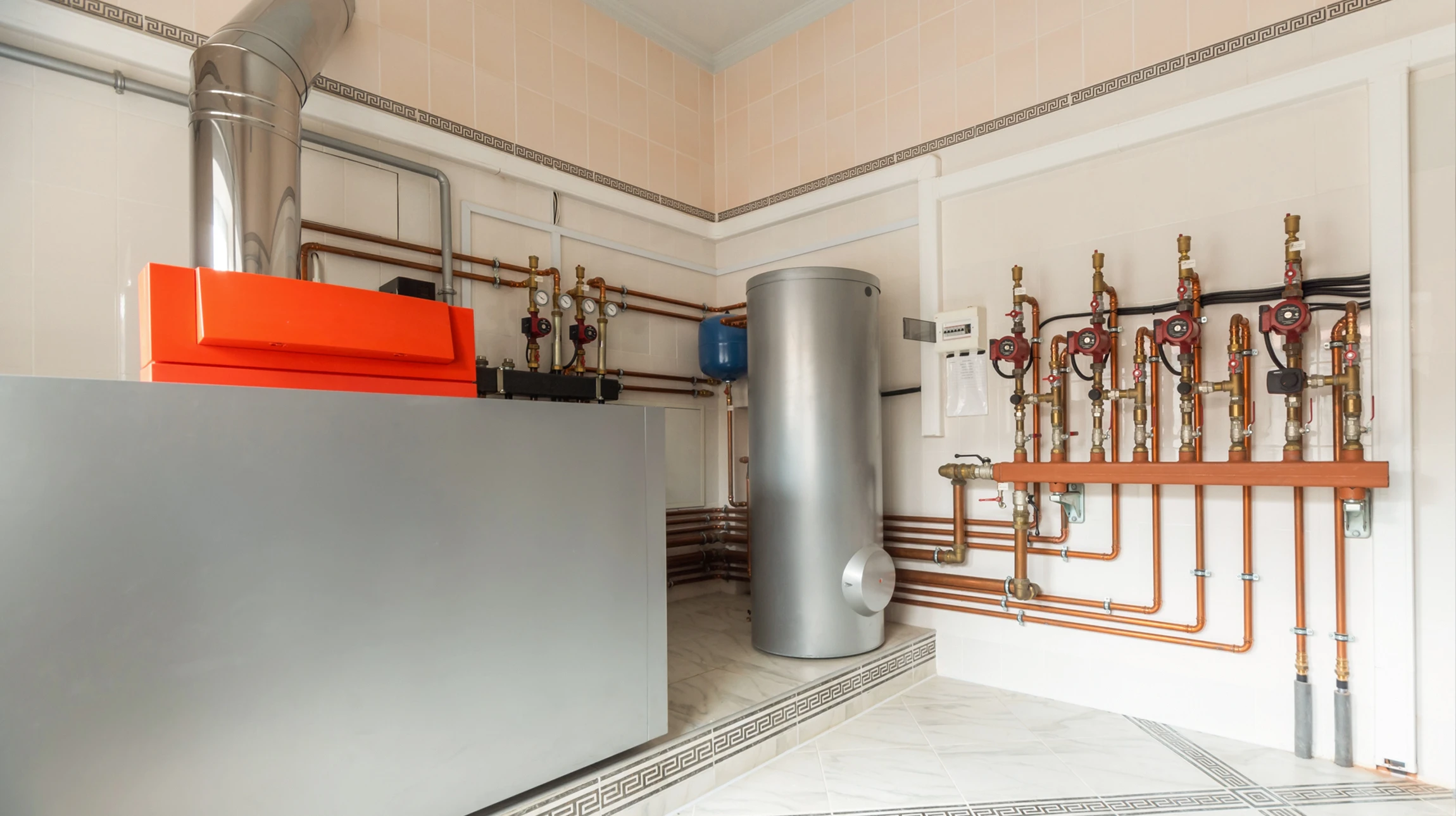 Un technicien en salopette ajuste une vanne sur une installation de chauffage en sous-sol