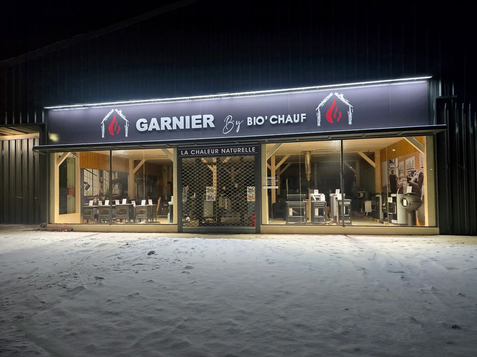 Intérieur lumineux et accueillant d'un showroom d'exposition de chauffage, avec plusieurs poêles à bois, poêles à granulés et cuisinières exposés côte à côte sur des socles ou intégrés dans des décors d'installation. Des clients en train de toucher, comparer et examiner les différents modèles. L'espace est spacieux, bien éclairé, avec des matériaux de qualité en évidence pour montrer la diversité des gammes disponibles. Ambiance professionnelle et accueillante.